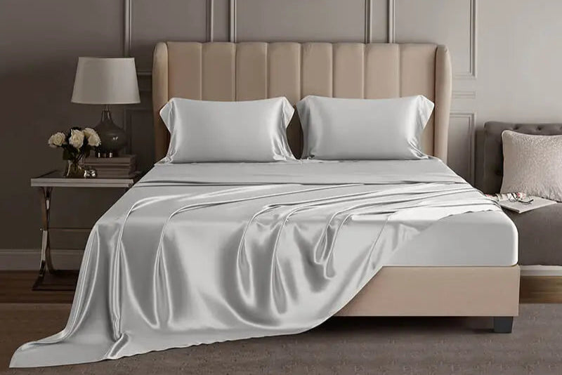Light grey mulberry silk sheet set on a bed in a luxury bedroom setting.
